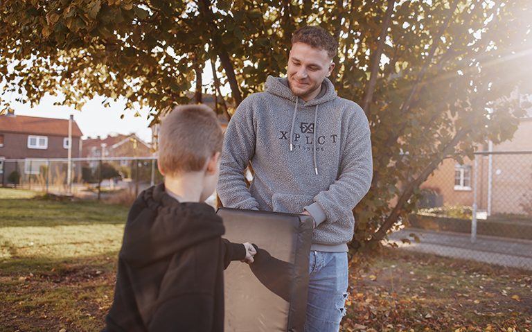Op de afbeelding is een van de diensten van Zorggroep HD te zien, namelijk de dienst 'training' ofwel weerbaarheidstraining. Je ziet een van de medewerkers van Zorggroep HD. Hij houdt de boksbal vast. De hulpvrager slaat met een vuist tegen het kussen aan.
